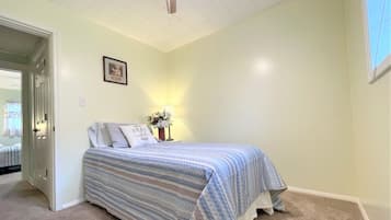 A bedroom with a bed, a nightstand, a framed picture on the wall, and a door leading to another room.