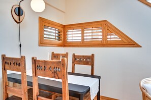 Un coin repas avec une table et des chaises en bois, un luminaire et une fenêtre dotée de volets en bois.