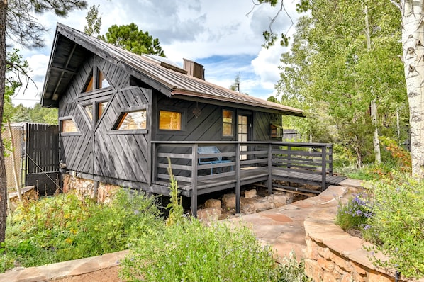 Une cabane rustique avec une façade en bois, une véranda et un chemin de pierre menant à l’entrée.