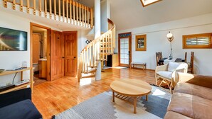 A spacious living area with a wooden staircase, a sofa, a round table, and wicker furniture. - Pet-Friendly Flagstaff Studio Cabin w/ Patio (Flagstaff)