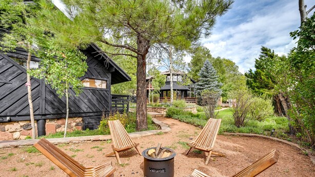 A rustic outdoor seating area with wooden chairs and a fire pit, surrounded by trees and a stone building. - Pet-Friendly Flagstaff Studio Cabin w/ Patio (Flagstaff)