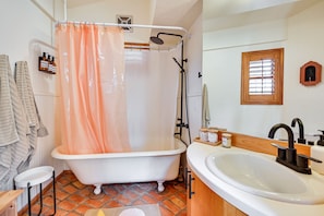 Une salle de bain avec une baignoire sur pieds, un lavabo blanc et une douche agrémentée d’un rideau de douche de couleur pêche.