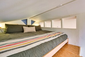 Une chambre à coucher avec un lit, des oreillers, une couverture à rayures, un plancher en bois et un plafond en pente.