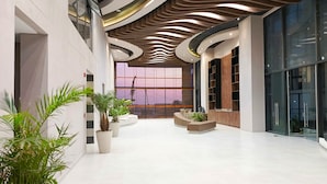 Een ruime lobby met een modern ontwerp, met een gebogen plafond, grote ramen en potplanten.