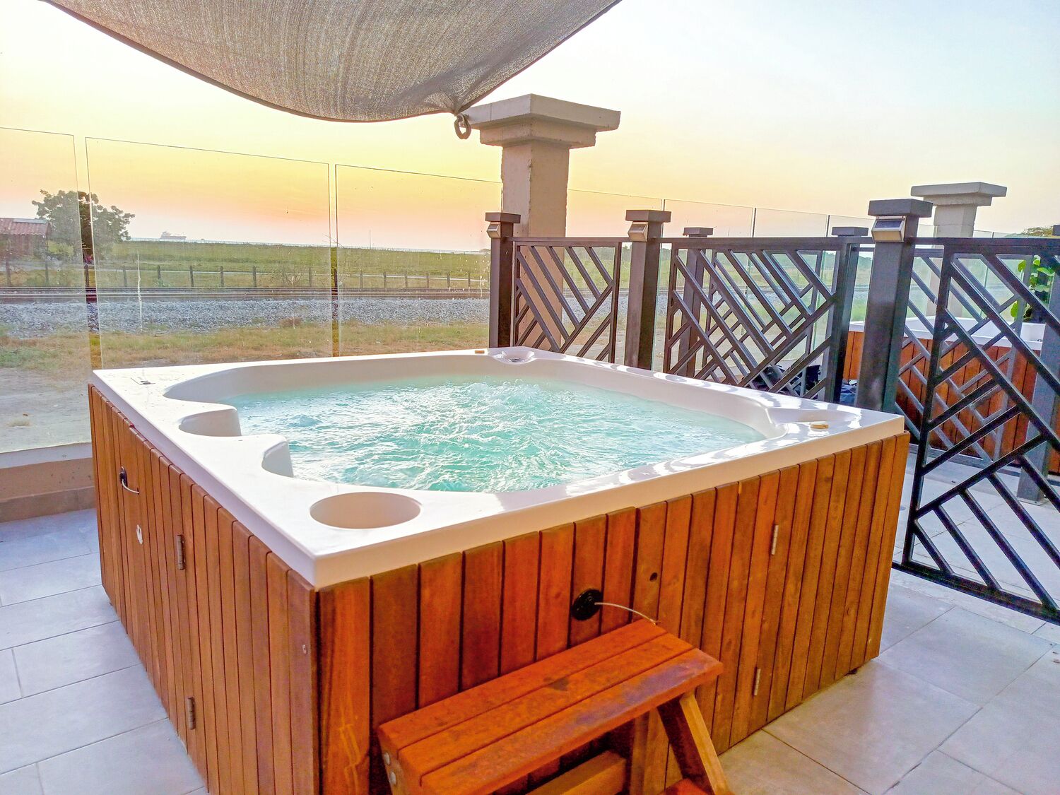 Ein hölzernes Whirlpool mit Sitzbank auf einem Balkon mit Blick auf ein Sonnenuntergangsfeld.