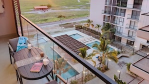 Een balkon met uitzicht op een zwembad, een klein tafeltje met een stoel, en een gebouw op de achtergrond.