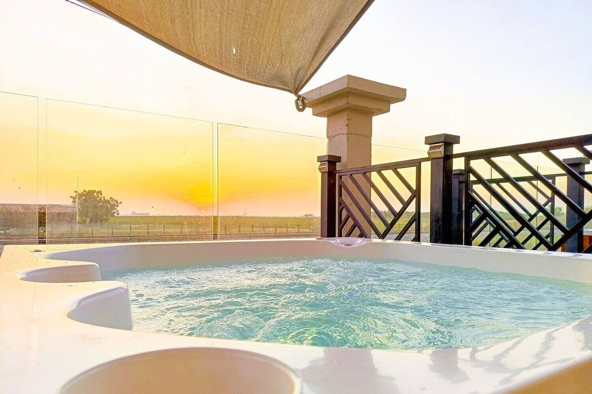 A hot tub with a view of the sunset, a pergola, and a railing.