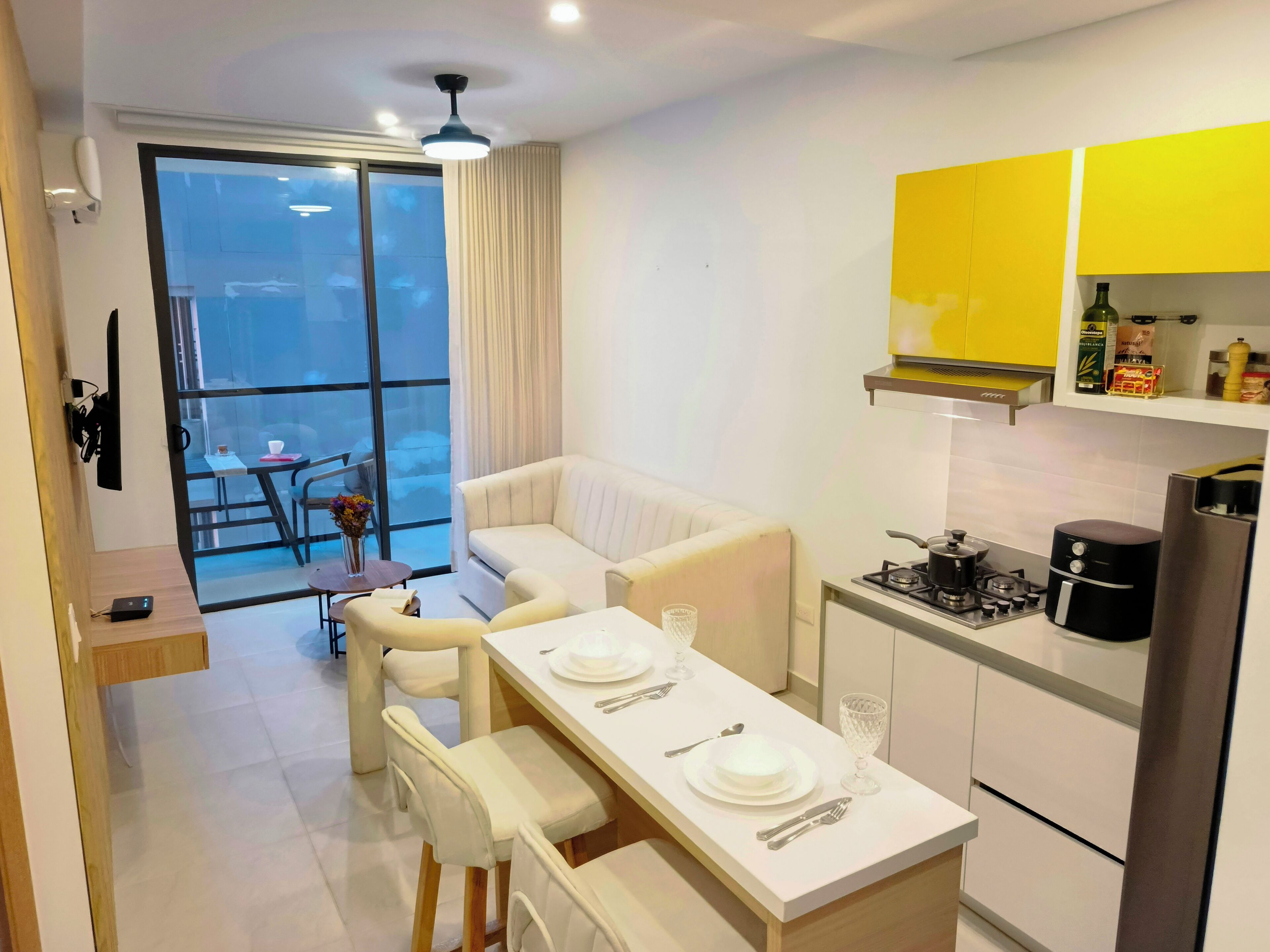 A modern kitchen with white cabinets, a dining table set for four, and a balcony with a view.