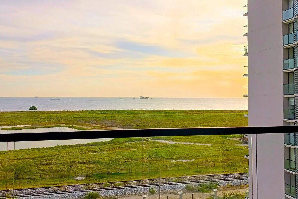 A view from a window overlooking a grassy area with a body of water and ships in the distance.