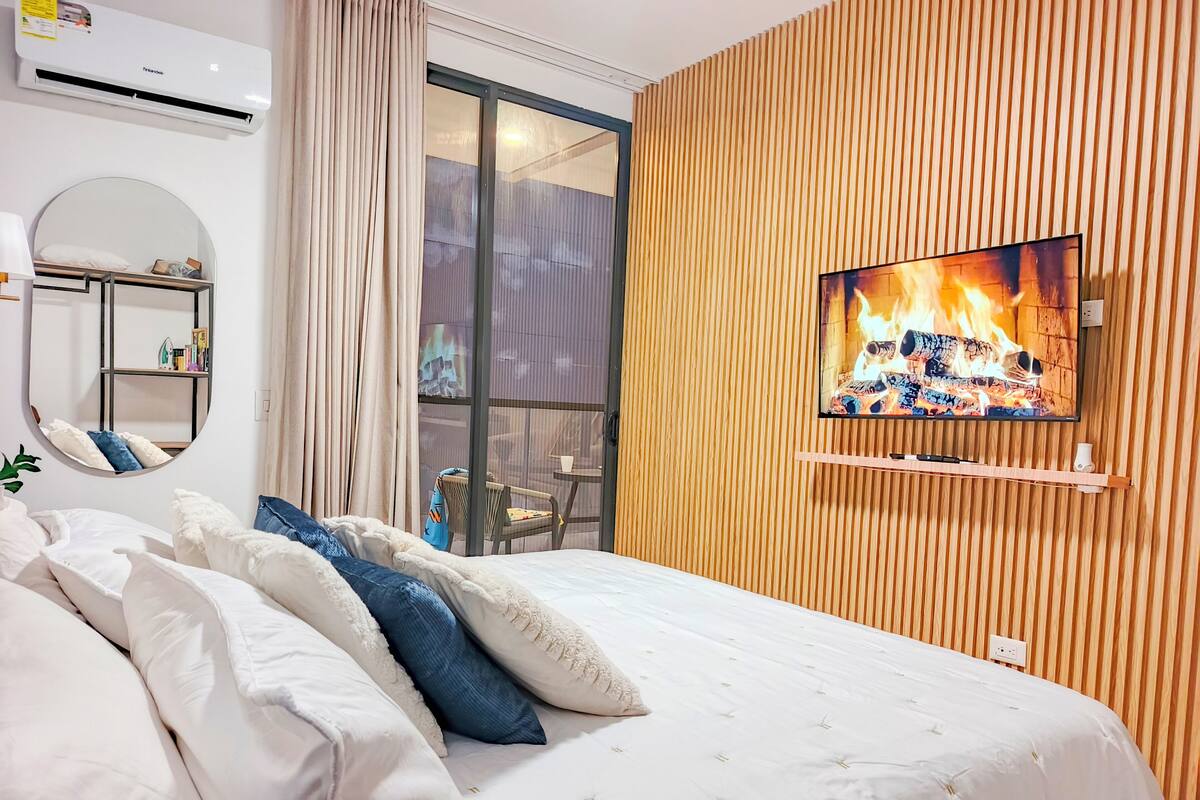 A bedroom with a bed, a TV, a mirror, and a window.
