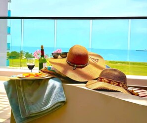 Een balkon met uitzicht op de oceaan, een fles wijn, een bord fruit en een strohoed.