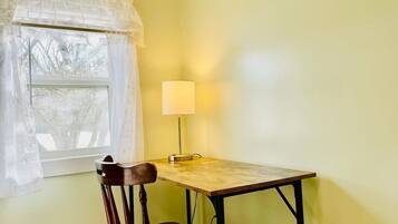 Een kleine kamer met een tafel, een stoel, een raam met dunne gordijnen en een bureaulamp.