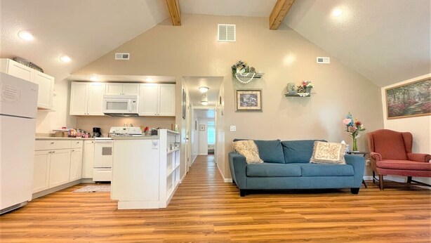 Amplia sala de estar con un sofá azul, un sillón rojo y una cocina con armarios blancos y un microondas.
