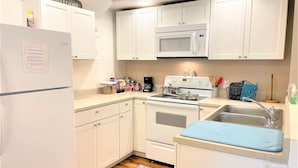 Cocina compacta con armarios blancos, microondas, estufa y lavabo.