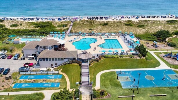 An aerial view of a resort with multiple swimming pools, a beach, and a parking area.