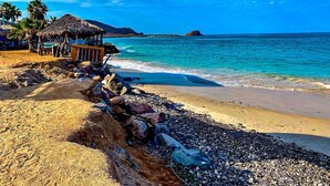 Ein Strand mit einer strohgedeckten Hütte, felsigem Ufer und klarem, blauem Meer.