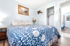 A bedroom with a bed, a nightstand, a wall-mounted shelf with flowers, and a door leading to another room. - Pontiac - Secluded Backyard, Pet Friendly (Fort Wayne)