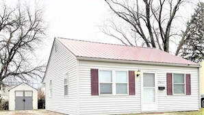 Une maison de plain-pied avec un toit rouge, un revêtement extérieur blanc et des volets rouges.
