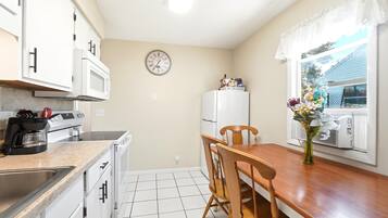 A compact kitchen with white appliances, a clock, and a dining area with a wooden table and chairs.