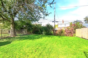 A backyard with a grassy lawn, a tree, and a wooden fence. - Pontiac - Secluded Backyard, Pet Friendly (Fort Wayne)