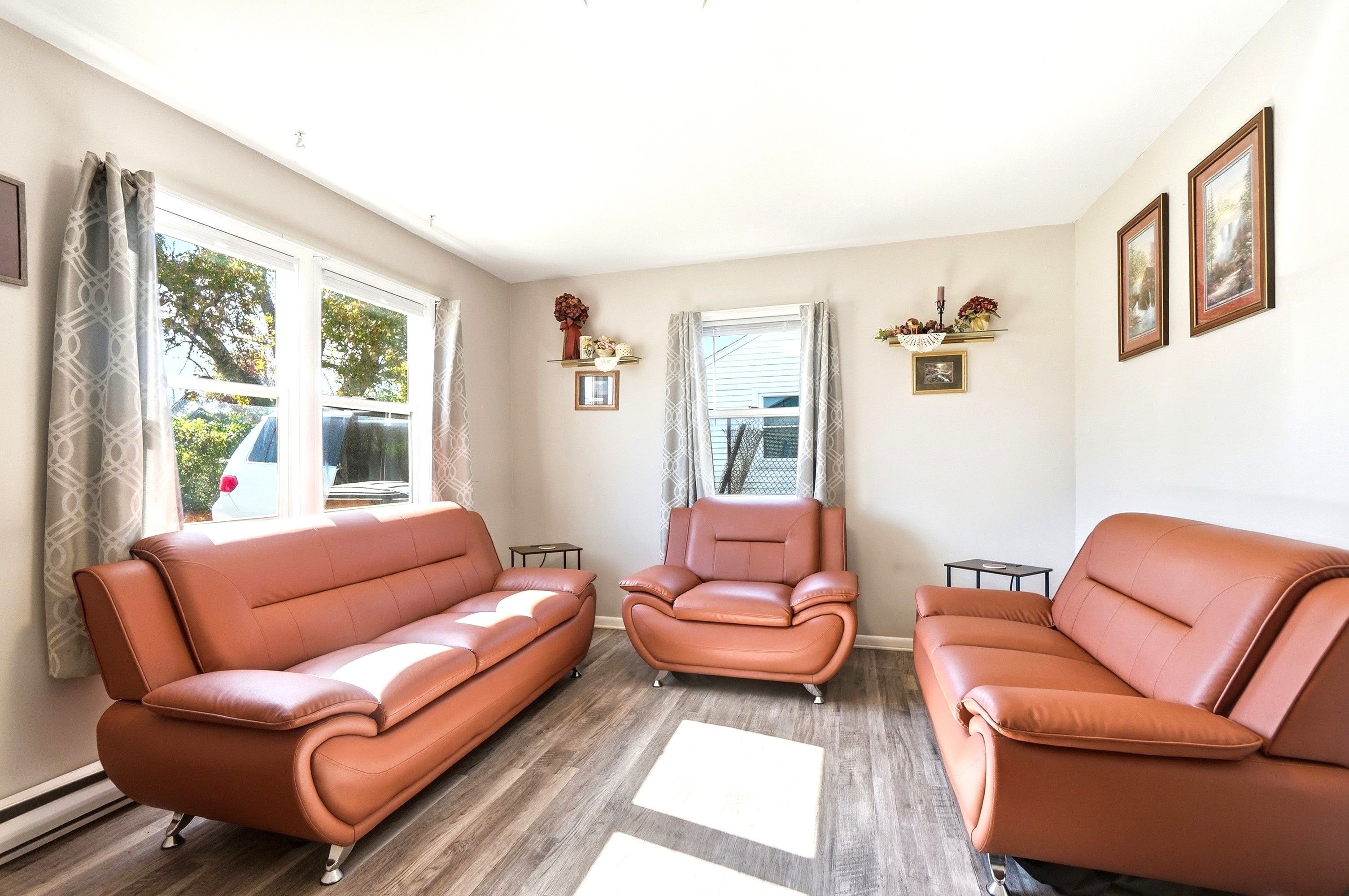 A living room with three leather sofas, a small table, and a wall-mounted shelf with decorative items.