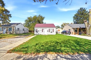 A residential area with a small house featuring a red roof, a front yard with a well-maintained lawn, and neighboring houses. - Pontiac - Secluded Backyard, Pet Friendly (Fort Wayne)