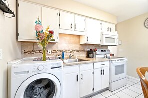 A compact kitchen with white cabinets, a washing machine, a microwave, and a sink. - Pontiac - Secluded Backyard, Pet Friendly (Fort Wayne)
