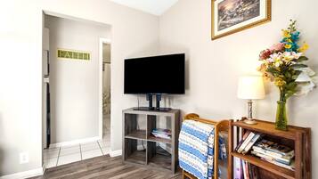 A room with a television on a stand, a bookshelf with books, a framed picture on the wall, and a sign with the word 'FAITH'.