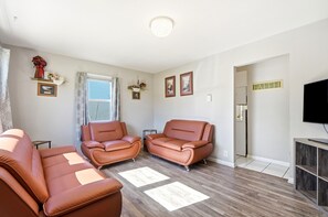A living room with two brown leather sofas, a flat-screen TV, and a wooden floor. - Pontiac - Secluded Backyard, Pet Friendly (Fort Wayne)