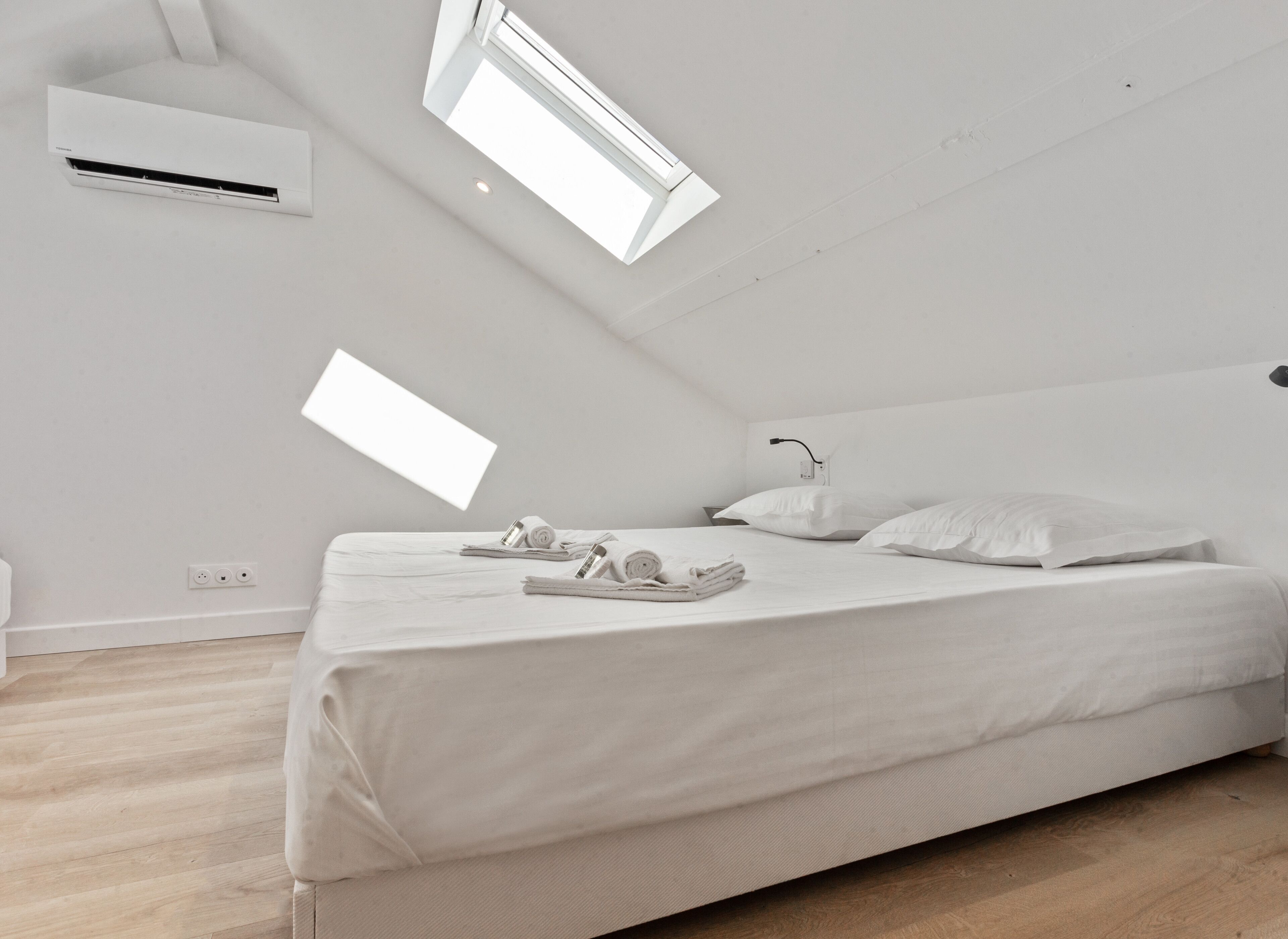 Une chambre à coucher moderne et minimaliste, avec un grand lit, deux oreillers et des serviettes soigneusement pliées.