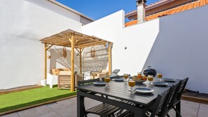 A patio with a table set for breakfast, a wooden pergola, and a white wall. - Maison Roccia - Welkeys (Anglet)