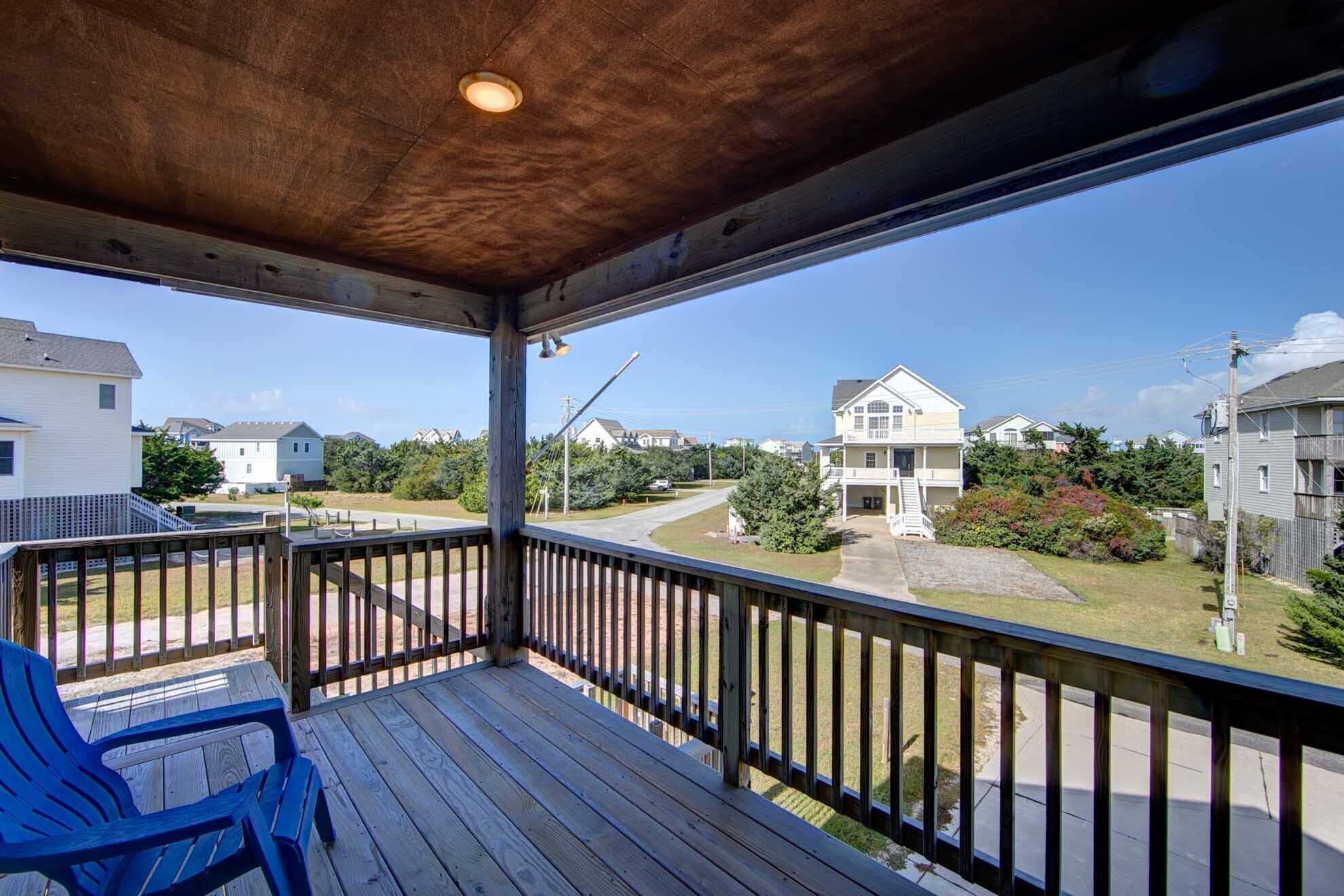 Una terraza de madera con barandilla, una silla azul y vistas a casas y vegetación.