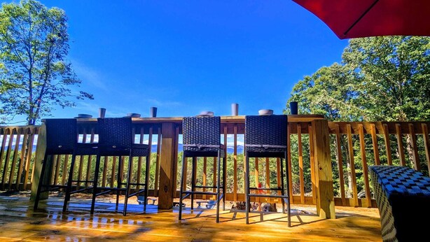 A wooden deck with outdoor seating, including chairs and a table, and a red umbrella. -  Sparrow Hawk Nest- Luxury Mountain View Tiny Home!  (Pickens)