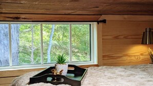 A room with a large window, a small potted plant, a black tray with decorative items, and a fluffy white rug. -  Sparrow Hawk Nest- Luxury Mountain View Tiny Home!  (Pickens)