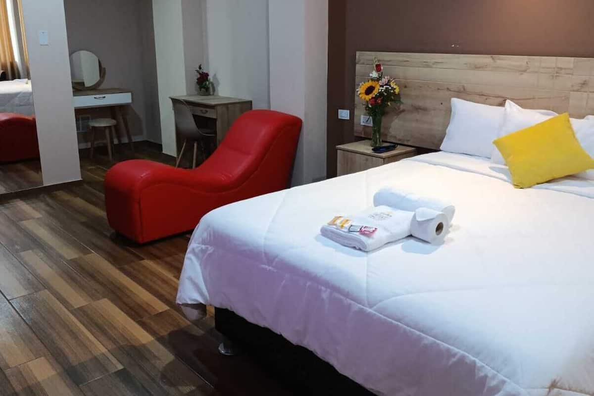 Hotellihuone, jossa on sänky, punainen tuoli, työpöytä ja peili.