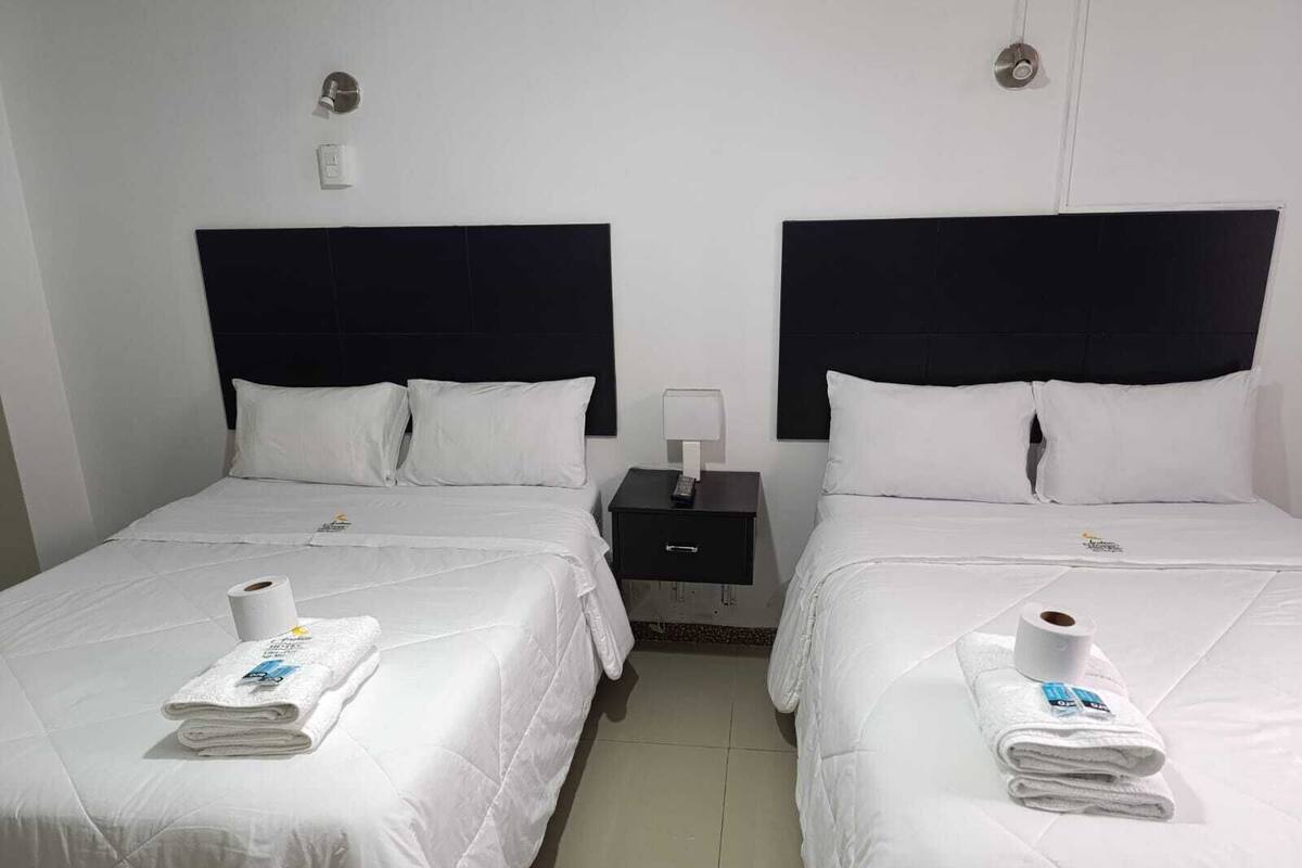 Hotellihuone, jossa on kaksi sänkyä. Jokaisessa sängyssä on valkoiset lakanat ja tyynyt, yöpöydällä on lamppu ja jokaisella sängyllä on pyyhe.