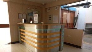 A reception desk with a glass top and wooden slats, a framed picture on the wall, and a door labeled "AFORO 11 PERSONAS". - Hotel Arabian (Lima)