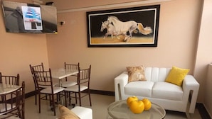 A living room with a white sofa, a dining table with chairs, a glass coffee table with lemons, and a painting of horses on the wall. - Hotel Arabian (Lima)