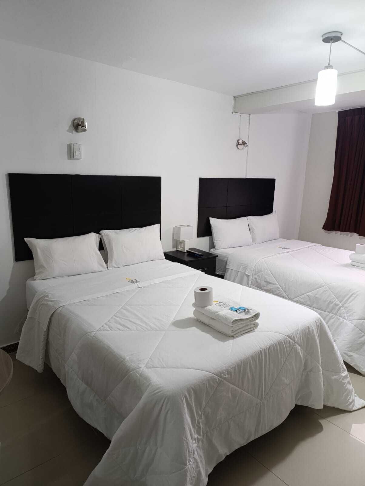 A hotel room with two beds, white bedding, a nightstand with a lamp, and a ceiling light.