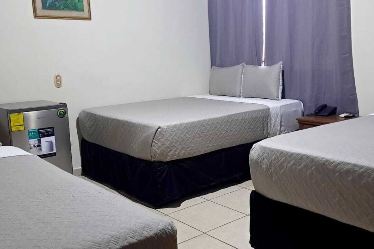A hotel room with two single beds, a desk with a computer, and a window with curtains.