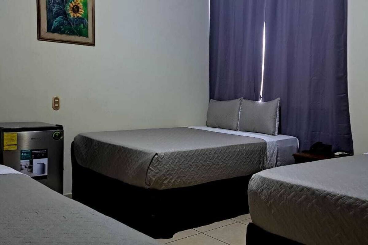 A hotel room with two beds, a desk, and a window with curtains.