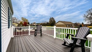 A wooden deck with a white railing, a rocking chair, and a patio table. - Game Room-Deck-Coffee Bar (Englewood)
