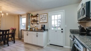 A kitchen with white cabinets, a granite countertop, a coffee station, and a microwave. - Game Room-Deck-Coffee Bar (Englewood)