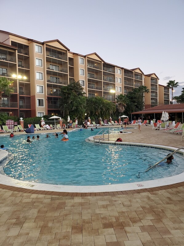 A hotel with multiple balconies, a swimming pool, and lounge chairs.