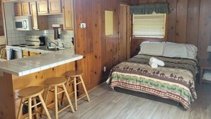 Interior de una cabaña con cocina, una cama y paredes de madera.