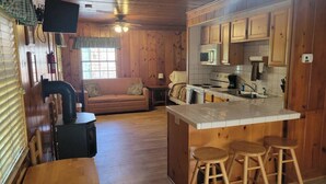 Un interior de cabaña acogedor con detalles de madera, una kitchenette, un sofá y un comedor.