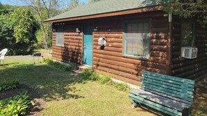 Una cabaña rústica de madera con puerta verde, buzón y banco exterior.