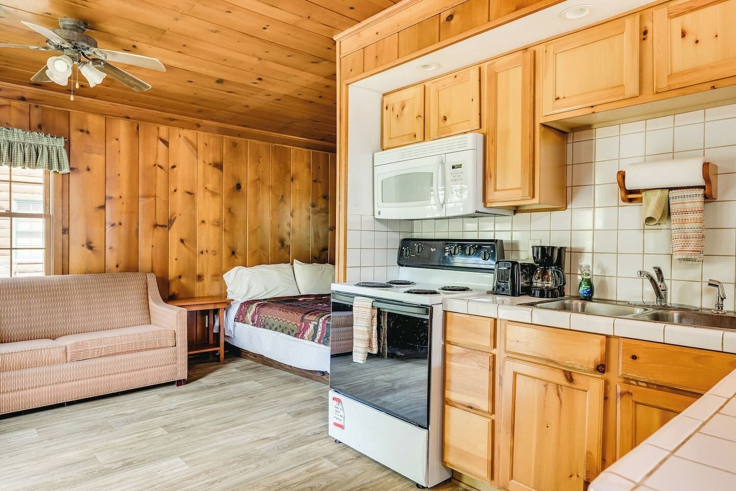 A compact kitchen with wooden cabinets, a microwave, stove, and a sink.