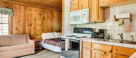 A compact kitchen with wooden cabinets, a microwave, stove, and a sink.