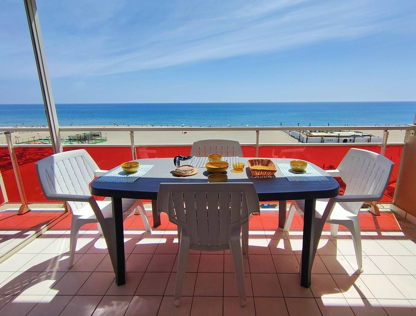 A balcony with a table set for two, overlooking a beach.